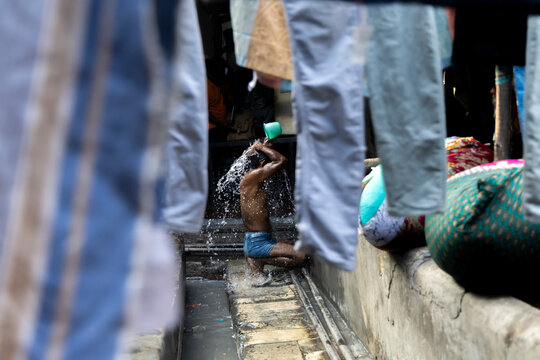 Man pouring water over himself behind hanging jeans at Dhobi Ghat, Maharashtra, Mumbai, India