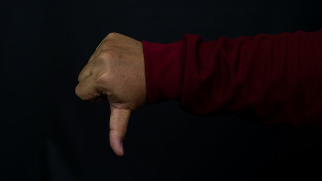 One human hand is pointed downward in a clear thumbs down gesture, indicating disapproval, failure, or rejection. That arm features a maroon long sleeved shirt, contrasting sharply