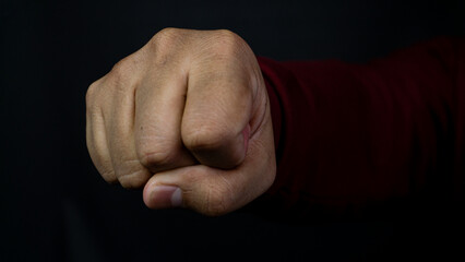 One single clenched human fist is directed straight toward the camera in a powerful striking motion. That arm belongs to an individual wearing a maroon long sleeved shirt, positioned © M. Faisal Riza