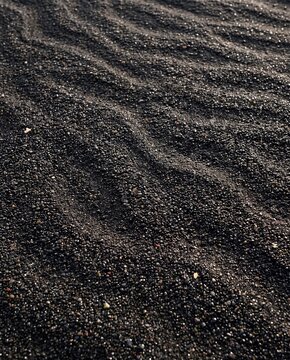 Natural textured volcanic black sand on a beach with wave patterns
