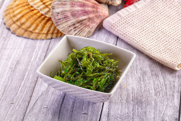 Rustic grey wooden table surface with white square bowl of green seaweed salad and scallop shells, Japanese appetizer © Andrei Starostin