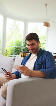 Man holding a blank card and a smartphone on a sofa at home