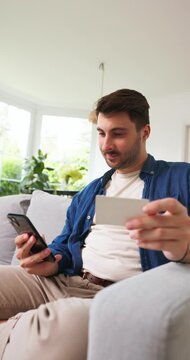 Smiling man using a smartphone on a sofa in a living room
