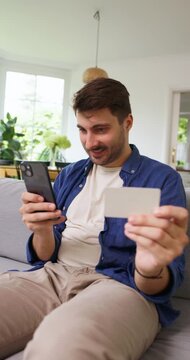 Man on a sofa smiling at a blank card he holds up