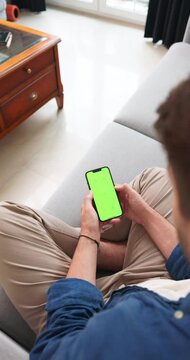 Man holding a smartphone with a green screen on a sofa