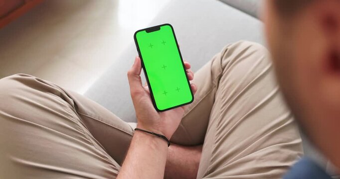 Man on a sofa looking at a green screen smartphone