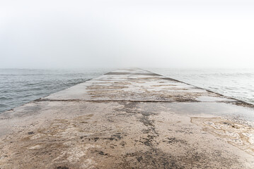 Naklejka premium A concrete pier extends into calm sea waters on a foggy day.