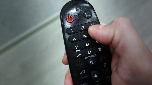 TV remote control, male finger presses power button, channels and volume buttons