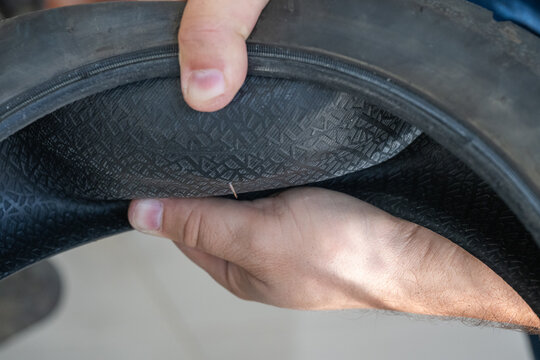 a mechanic inspecting the inside of a bicycle or electric scooter tire and pointing out a sharp thorn causing a flat puncture.