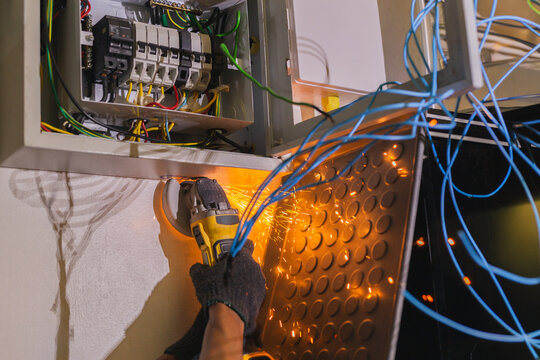 Electrician using an angle grinder with flying sparks during maintenance.