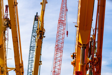 Construction cranes with yellow telescopic booms beside red and green lattice booms beneath a blue sky, hydraulic cylinders and suspended hooks on heavy lifting equipment for crane rental businesses. © Fahroni