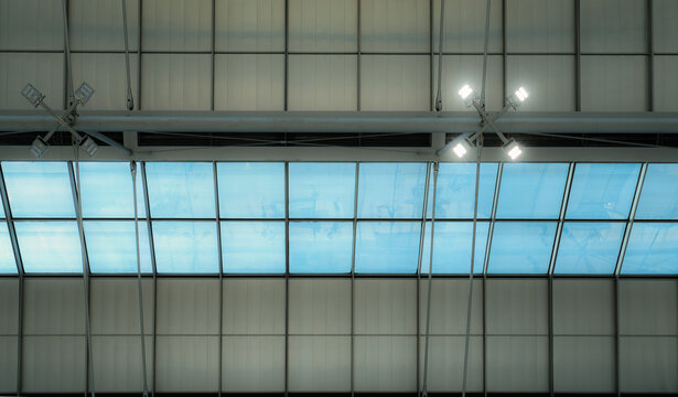 Airport roof with glass skylights and ceiling mounted LED lamps, rectangular panes framed by metal supports beside panels, modern interior architecture combining glazing and energy saving lighting.