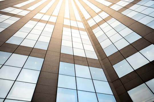 Upward view of a facade with vertical columns and rows of windows catching sunlight in La Defense near Paris France creating a repeating architectural pattern