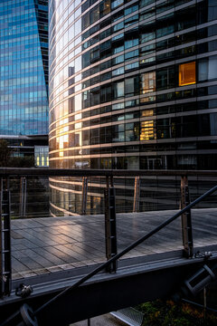 Sunlight catches glass office towers behind a raised walkway with railings in La Defense near Paris France creating reflections between buildings in the district