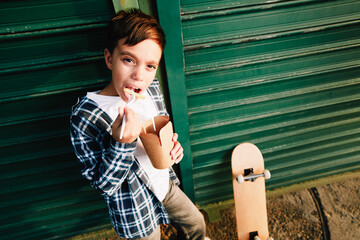 Young Caucasian schoolboy eating noodles from a takeaway container while standing beside his skateboard © djile