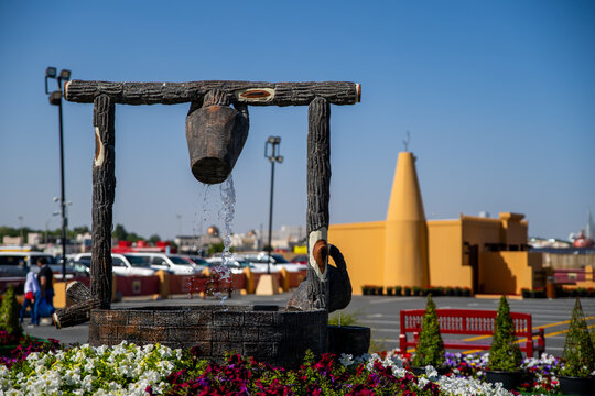 The Splendor of Qatari Heritage and Natural Harmony: A rustic wooden water well sculpture flowing with fresh water, centered within a rich circular bed of purple and white petunias