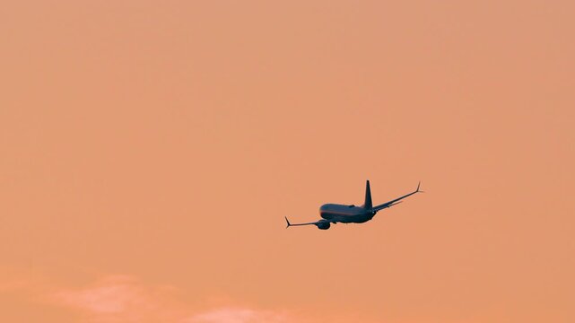 A passenger jet climbs through a vibrant golden hour sky after takeoff. This minimalist scene represents global travel, logistics, and aviation industry growth.