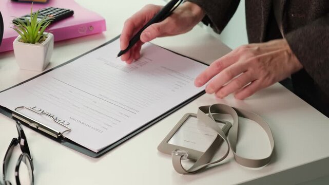 Legal document and administration concept. Close hands holding a pen over a clipboard, reading and analyzing printed paperwork in a office environment.