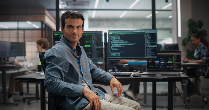Portrait of Confident Caucasian Male Tech Specialist at Desk With Multiple Monitors Showing Code and Laptop in Modern Office, Developing Software Solutions for Business Growth, Working Using Computer