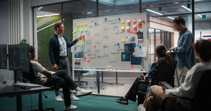 Male Project Manager Explaining Deep Learning Algorithm Architecture on Whiteboard While Meeting and Talking With Multiethnic Team of Software Developers and Data Analysts in Modern Office