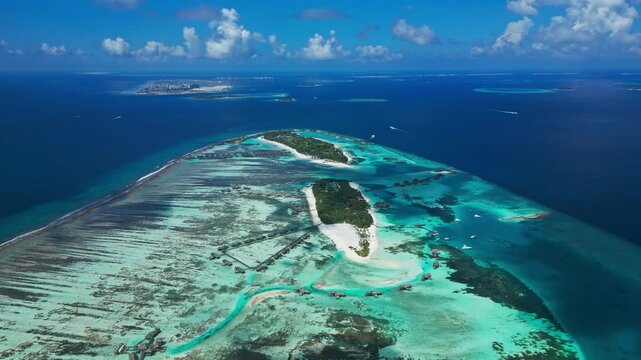 Panoramic drone shot of luxury island resort surrounded by turquoise coral reef lagoon and deep ocean. Perfect establishing background for travel agency and cruise promo.Maldives