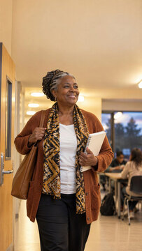 Smiling senior black woman with braids walking in school corridor holding notebook with leather bag, happy mature student at evening college