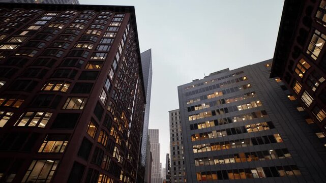dusk urban canyon of lit offices. towering brick and glass facades, warm interior lights glowing, narrow street perspective, overcast sky, cinematic lowangle
