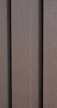 Dark brown HDPE plastic lumber fence surface with alternating projecting and recessed boards, narrower inset slats, slight texture, and numerous tiny white flecks in a vertical close-up view