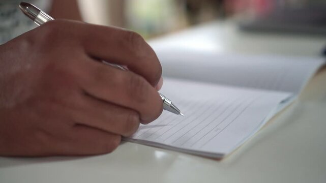 hand holding a pen, hesitating before writing on a lined notepad. Decision making, writer's block and contemplation concept.