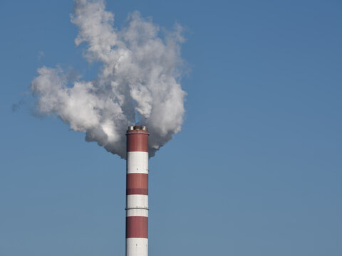 Power plant chimney with a visible flue gas plume against blue sky and wide copy space, suitable for energy, industry and environmental themes.