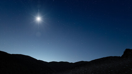 Fototapeta premium Glowing Christmas star above a peaceful mountain landscape