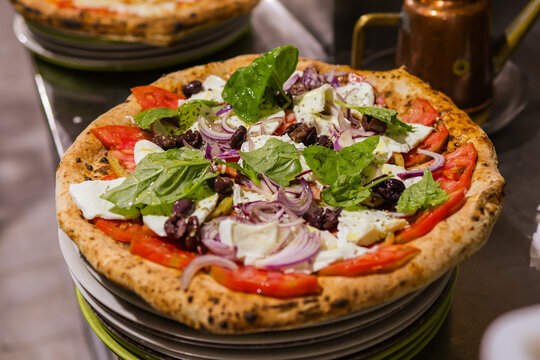 Gourmet pizza topped with fresh tomatoes, mozzarella cheese, red onion, black olives and basil leaves.