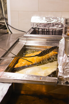 Traditional folded pizza being deep fried in hot oil inside a professional fryer, with bubbling oil and kitchen utensils.