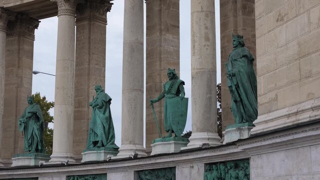 Bronze statues of historical Hungarian leaders stand between monumental stone columns at Heroes' Square in Budapest