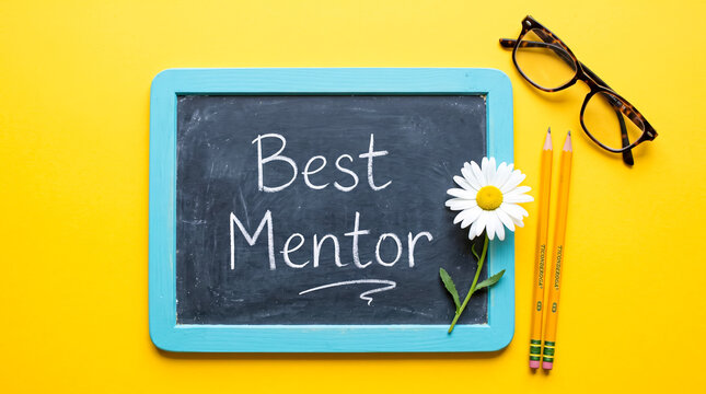 Creative chalkboard with Best Mentor text surrounded by pencils, glasses, and daisy on yellow background