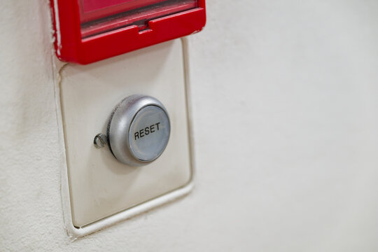 Metallic reset button on white wall with red protective cover in building