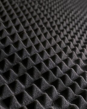 Close-up of black acoustic foam with repeating pyramid-shaped peaks and deep shadows, sound absorbing material texture for recording studio design, noise reduction and industrial backgrounds