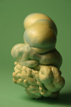 A close-up studio shot of an abstract biomorphic sculpture made of expanded foam, featuring a smooth pastel yellow and blue gradient top against a solid green background.