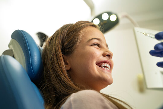 A young girl smiles and stays calm in a dental chair while a dentist prepares for intervention 