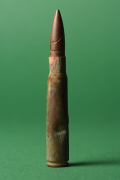 A macro studio shot of an old, damaged military bullet standing vertically against a solid green background, symbolizing the raw reality of war and conflict.