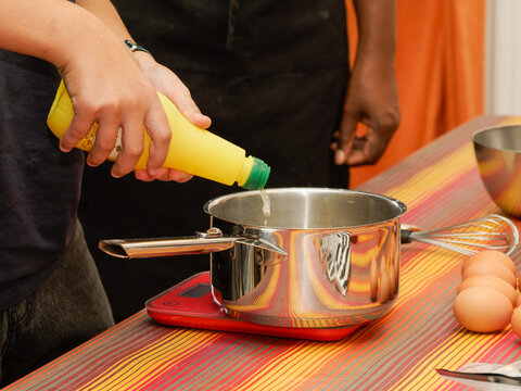 Main versant un liquide jaune dans une casserole en cuisine