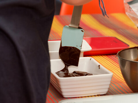Personne versant un liquide chocolat&eacute; ou une p&acirc;te fonc&eacute;e dans un r&eacute;cipient blanc