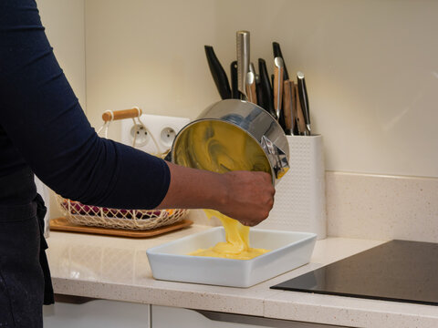 Main versant une p&acirc;te jaune dans un plat blanc sur un plan de travail de cuisine