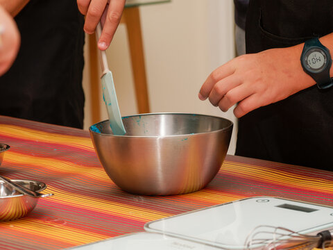 Gros plan sur des mains pr&eacute;parant un aliment dans un bol en inox sur une table &agrave; rayures color&eacute;es