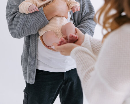 Father holds newborn baby while mother gently touches small feet in cozy room.