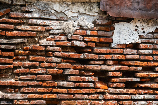 Textured wall background of exposed weathered red clay bricks with peeling plaster mortar.