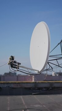 White satellite dish remains mounted on an urban building rooftop under a clear blue sky. The satellite dish installation provides clean telecommunications context for mobile media.