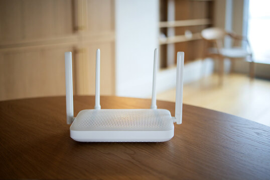 White wireless router with four upright antennas on polished wooden table in softly lit modern home interior, shallow depth of field, household networking equipment