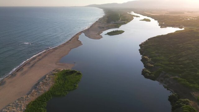Panoramic aerial view of the mouth of the Coghinas River, where it flows into the sea at San Pietro a Mare in Sardinia, featuring an elongated sandy spit, a small green islet, and hills