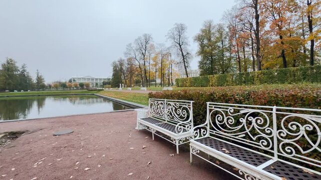 White benches rest beside a tranquil pond in Catherine Park, Pushkin. This smooth pan shot in slow motion evokes a serene and melancholic mood.